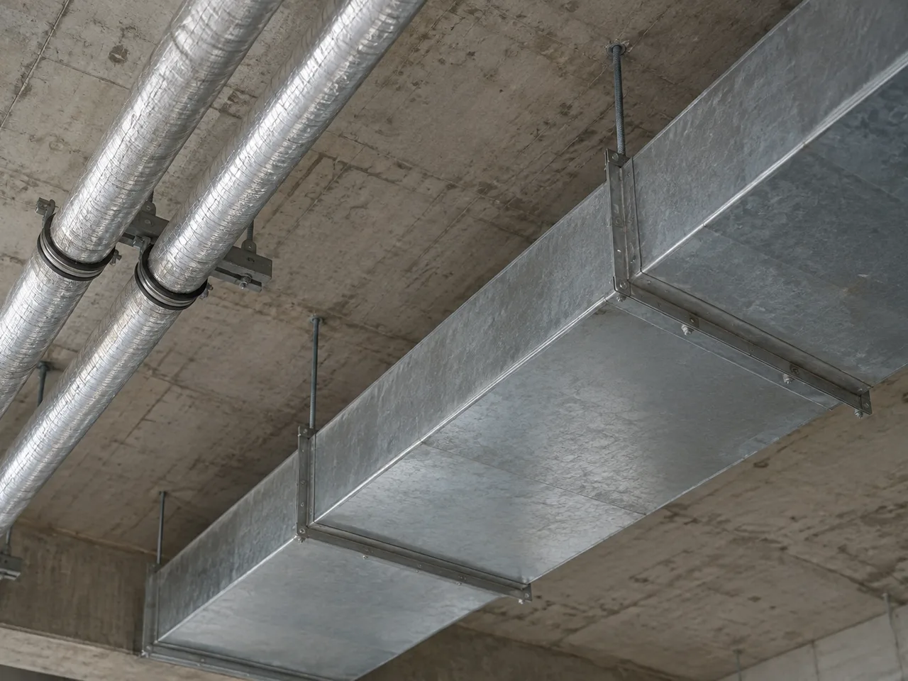 Illustrative galvanised duct and insulated pipework suspended beneath a concrete soffit