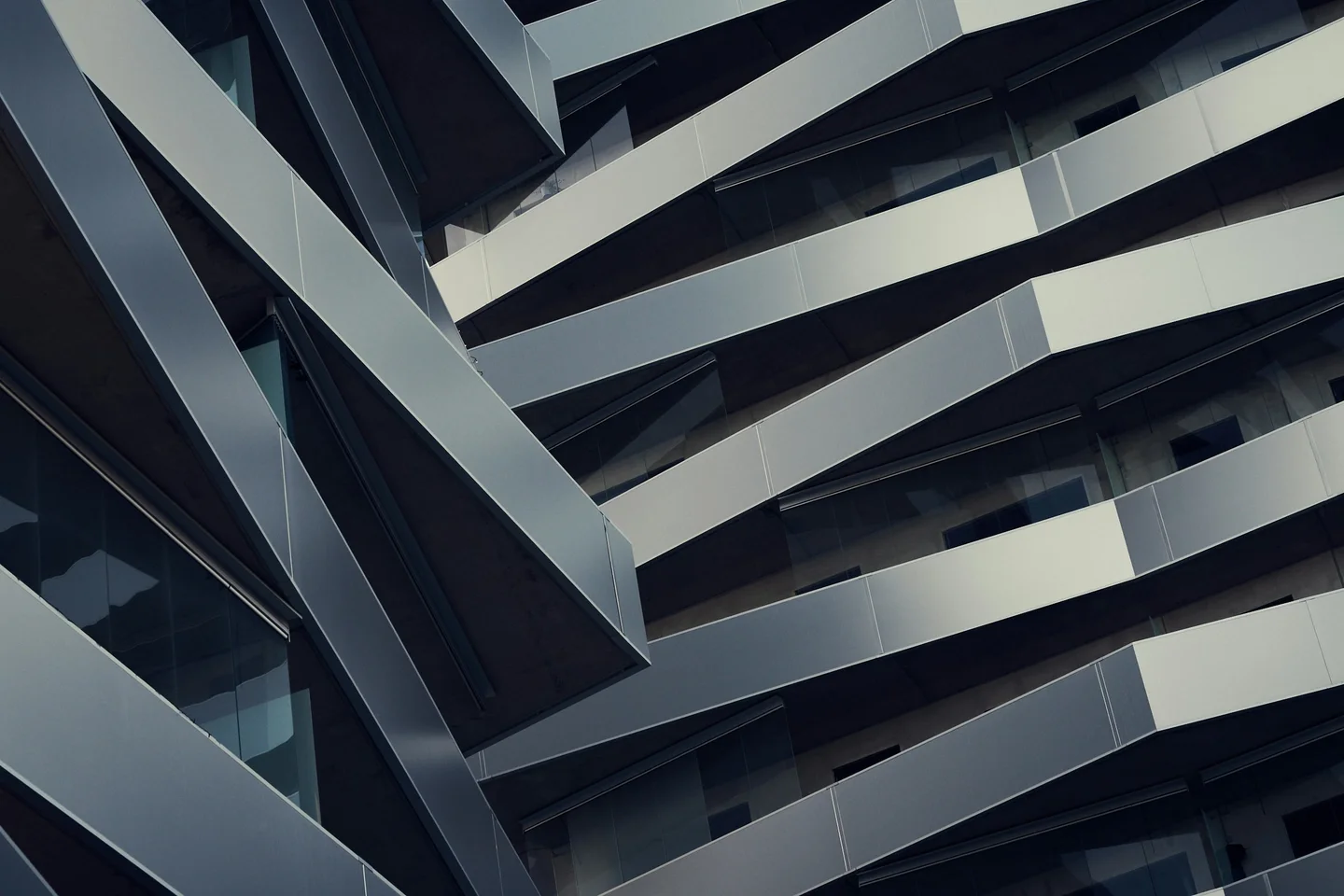 Close oblique view of folded silver facade panels and recessed dark glazing