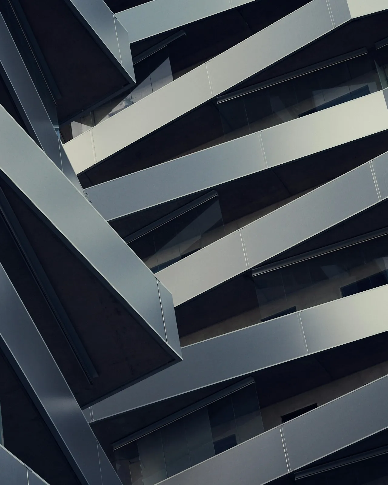 Close oblique view of folded silver facade panels and recessed dark glazing