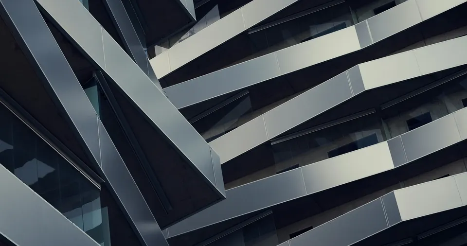 Close oblique view of folded silver facade panels and recessed dark glazing