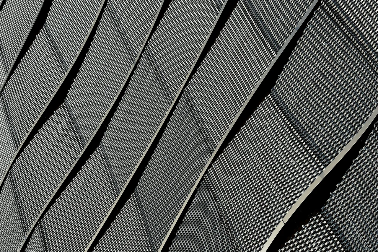 Close view of curved perforated metal facade panels with staggered vertical joints